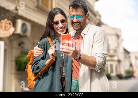 I giovani turisti hipster alternativi sono una coppia innamorata di passeggiare all'aperto lungo la strada della città, abbracciandosi e indossando un guardaroba moderno e alla moda. Fashi Foto Stock