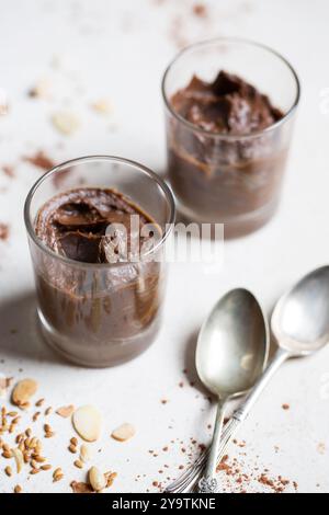 Mousse di cioccolato all'avocado in pentole di vetro con cacao e noci, dessert cremoso senza latticini, indulgenza sana su sfondo chiaro. Foto Stock