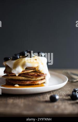 Frittelle di banana con yogurt e mirtilli, sciroppo d'acero versato su pila su un piatto bianco, una deliziosa colazione. Foto Stock