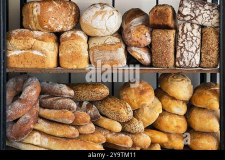 Pani artigianali assortiti impilati sugli scaffali dei prodotti da forno, lievitazione naturale, pane rustico e seminato, esposizione giornaliera appena sfornata. Foto Stock
