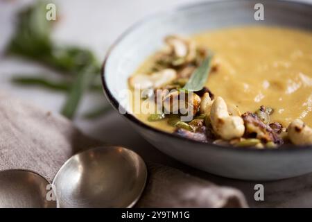 Zuppa di cavolfiore arrosto servita in un recipiente di ceramica grigia con anacardi tostati e semi di zucca. Foto Stock