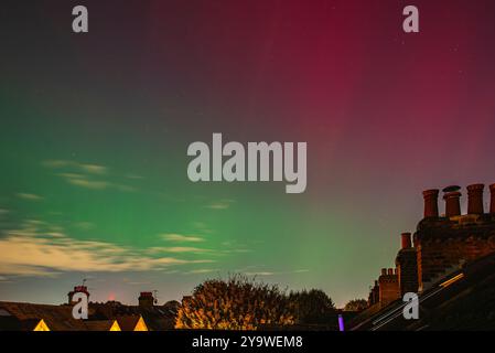 Colori rosso, verde e viola dell'aurora boreale, vista sui tetti e sui camini di una strada suburbana, West London Foto Stock