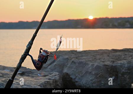 Il pescatore è pronto a pescare all'alba mentre il sole del mattino risplende sull'acqua del lago Foto Stock