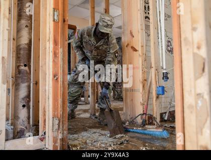 Marshall, Stati Uniti. 10 ottobre 2024. Peakpellem Laoukpessi, assegnato al 502nd Infantry Regiment, raschia il fango da un pavimento del magazzino danneggiato in seguito all'uragano Helene, 10 ottobre 2024 a Marshall, Carolina del Nord. Crediti: PFC. Cristian Lopez/US Army Photo/Alamy Live News Foto Stock