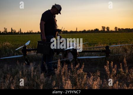 Pilota drone agricolo che sostituisce le batterie al crepuscolo. Foto Stock