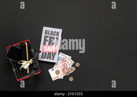 Biglietto d'auguri con testo IN VENDITA DEL BLACK FRIDAY, carrello, regali, carte di credito e denaro su sfondo scuro Foto Stock