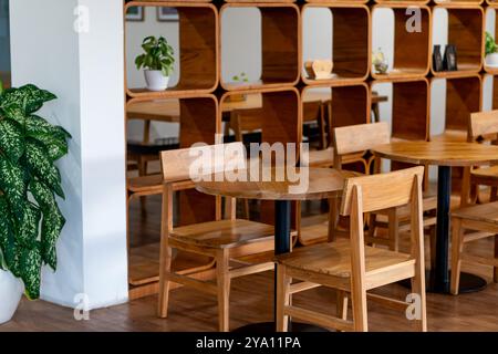 Un intimo caffè interno caratterizzato da tavoli e sedie in legno. Il design include un ripiano in legno sullo sfondo, decorato con piante e decorazioni Foto Stock