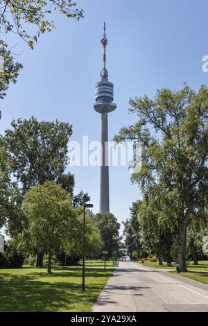 L'alta torre di trasmissione sovrasta gli alberi nel parco municipale sotto un cielo blu, Vienna Foto Stock