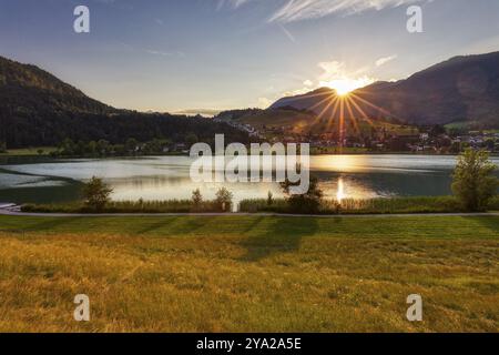 Tramonto su un lago con montagne e prati, luce radiosa e riflessi sull'acqua, Thiersee Foto Stock