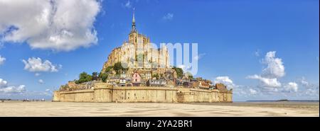 Vista panoramica di un'abbazia monumentale arroccata su un campo sabbioso sotto un cielo blu, le Mont-Saint-Michel Foto Stock