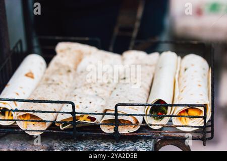 Focaccine arrotolate e ripiene di formaggio e verdure. Preparazione del barbecue all'aperto. Cibo di strada vegetariano su una griglia di metallo da vicino. Foto Stock