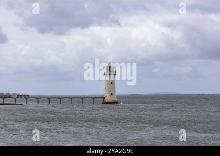 Un faro solitario sorge nell'acqua sotto un cielo nuvoloso, circondato dal mare, il faro di Tarbert Foto Stock