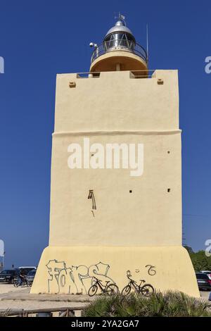 Faro giallo con graffiti sulla base di fronte a un cielo azzurro e biciclette parcheggiate, Frontera Foto Stock