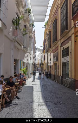 La gente passeggia attraverso un vicolo ombreggiato e stretto circondato da edifici in vecchio stile, Siviglia Foto Stock