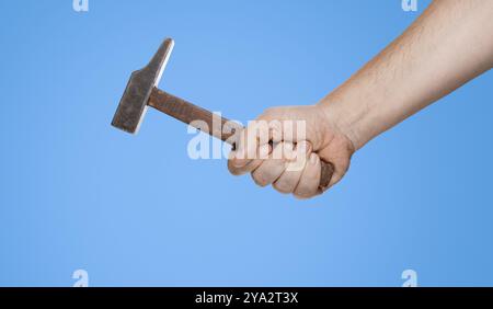 Uomo che tiene un martello in mano davanti a uno sfondo blu Foto Stock