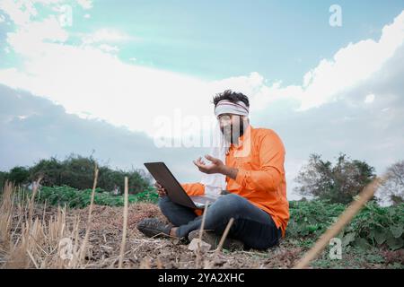 Agricoltore rurale indiano che lavora su un computer portatile nel campo delle colture Foto Stock