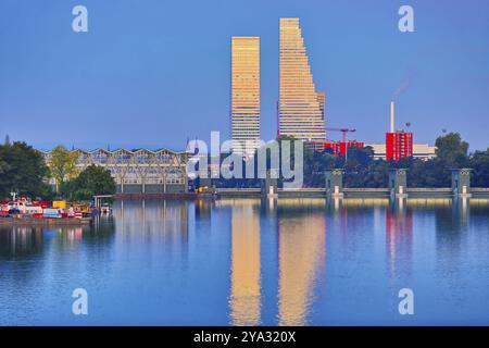 Grattacieli moderni che si riflettono nel fiume alla luce della sera accanto a uno sfondo urbano, Roche Towers, Hoffmann- la Roche, l'edificio più alto di Switze Foto Stock