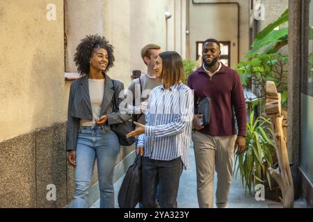 Gruppo di diversi colleghi maschi e femmine che escono dal coworking parlando e sorridendo Foto Stock