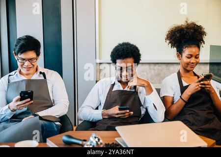 Un gruppo diversificato di baristi si è riunito in un bar utilizzando il telefono per rilassarsi. Professionisti in Foto Stock