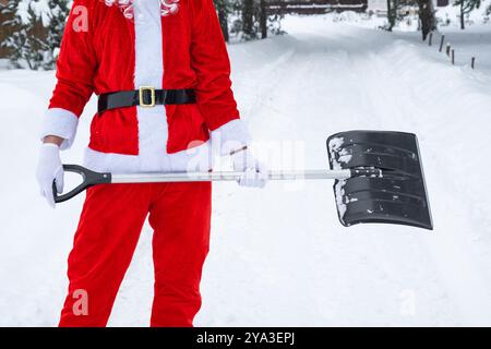 Babbo Natale pulisce la neve con la pala in inverno all'aperto dopo una nevicata. Pulire le strade del villaggio, pulire il passaggio per le auto, difficile Foto Stock