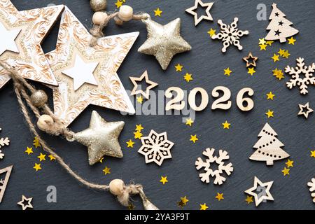 Felice anno nuovo: Lettere in legno e numeri 2026 su sfondo nero festoso con paillettes, stelle, neve. Saluti, cartolina. Calendario, copertura Foto Stock