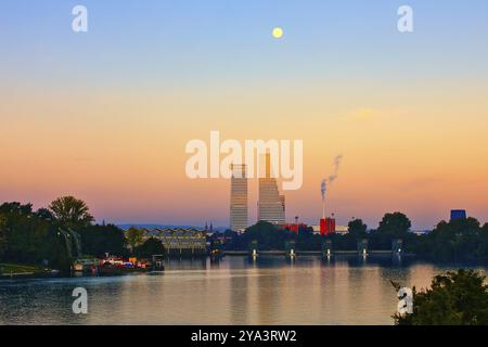Paesaggio fluviale al tramonto con grattacieli e luna piena. La scena contiene accenti naturali e industriali, Roche Towers, Hoffmann- la Roche, le più alte Foto Stock