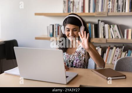 Allegro giovane allenatore indiano in cuffie salutando il laptop Foto Stock