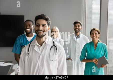 Felice giovane medico di sesso maschile che posa di fronte a colleghi amichevoli Foto Stock