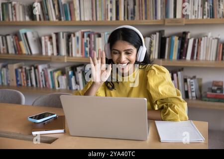 Felice giovane insegnante indiano in cuffie salutando il laptop Foto Stock