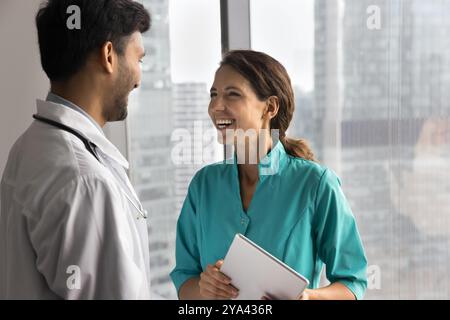 Una giovane infermiera sorridente chiacchiera con un medico di sesso maschile per finestra Foto Stock