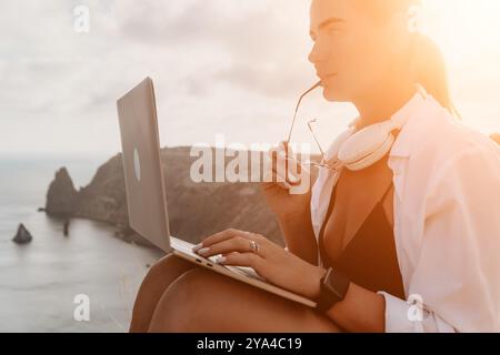 Donna laptop Sunset Beach: Giovane donna che lavora con un laptop mentre si gode la vista del tramonto dalla scogliera. Foto Stock