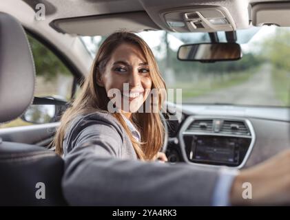 Bella giovane donna che guida un'auto e guarda dietro le spalle, concetto di guida sicura Foto Stock