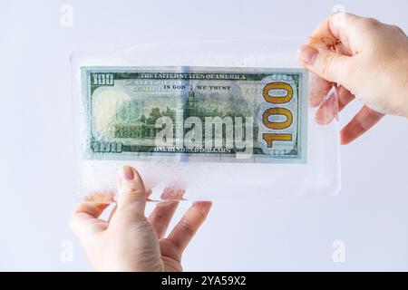 100 dollari congelati sotto uno strato di ghiaccio nelle mani per motivi di progettazione Foto Stock