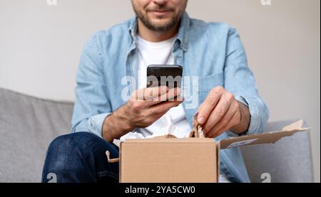 Uomo che riceve, disimballa e fotografa il suo acquisto online. Foto Stock