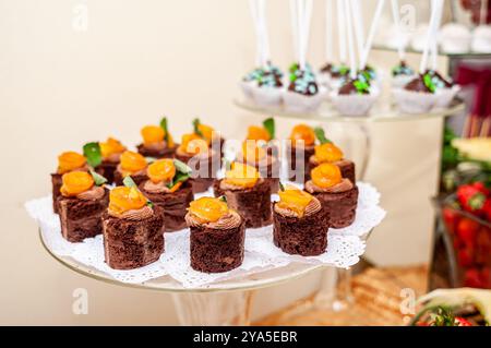 Deliziosi bocconcini di brownie al cioccolato con topper di albicocca glassati deliziosamente disposti su un tavolo di dessert natalizi. Foto Stock