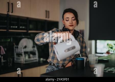 Donna che versa il tè in una cucina moderna con le cuffie Foto Stock