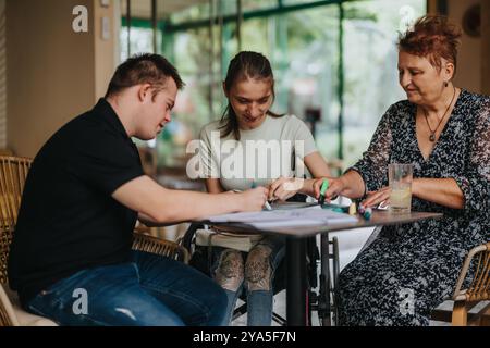 La donna anziana assiste il giovane uomo e la ragazza con disabilità nell'attività artistica Foto Stock