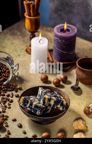 Due barrette di sapone naturale in un ambiente spa circondato da chicchi di caffè, noci di macadamia, zucchero di canna e candele accese Foto Stock