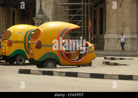 L'Avana, Cuba 2024 aprile. L'autista si prende una pausa, riposando nel suo taxi giallo di cocco parcheggiato di fronte al Gran Teatro de la Habana, in attesa dei clienti Foto Stock