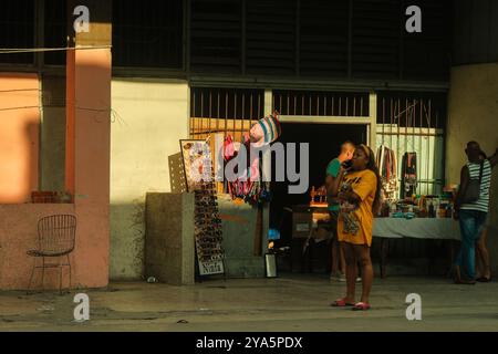 L'Avana, Cuba 2024 aprile. Donna cubana al telefono cellulare di fronte a un negozio locale che vende prodotti quotidiani e souvenir. Cuba sta affrontando una crisi economica ora. Foto Stock