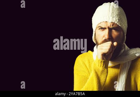 Uomo barbuto malato che tossisce. Tosse cronica. Uomo malato con maglione, cappello e sciarpa che tossisce dal freddo. Tosse con polmonite, bronchite, allergia, asma, COP Foto Stock