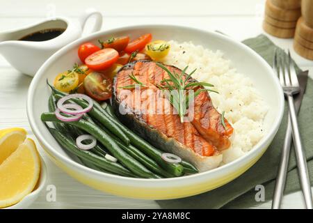 Gustosa bistecca di salmone alla griglia con riso e verdure su un tavolo di legno bianco, primo piano Foto Stock