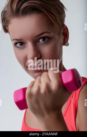 Una giovane donna determinata solleva i manubri rosa in una palestra, mostrando la sua forza e motivazione, ispirando uno stile di vita sano e attivo Foto Stock