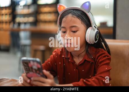 Una ragazza con le cuffie per orecchie di gatto usa il suo telefono per musica o giochi Foto Stock