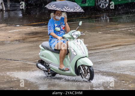 SAMUT PRAKAN, THAILANDIA, ottobre 03 2024, Una donna con un ombrello guida una moto sotto la pioggia Foto Stock