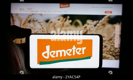 Persona che tiene un cellulare con il logo dell'organizzazione alimentare biologica tedesca Demeter sullo schermo di fronte alla pagina web. Mettere a fuoco il display del telefono. Foto Stock