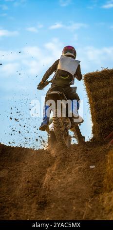 Un pilota di motocross che controlla la sua moto in cima a una collina che solleva fango e sporcizia dalla ruota posteriore di knobby su una pista sterrata in collina durante un fuoristrada Foto Stock