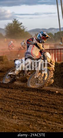 Pilota di motocross in azione che gira la sua motocicletta fangosa su una curva stretta su terreno bagnato, durante una gara di resistenza all'aperto. Foto Stock