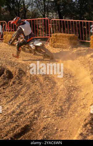 Un pilota di motocross si piega con la gamba allungata mentre affronta una curva acuta su una pista sterrata, gettando polvere e ghiaia dalla sua ruota posteriore che slitta. Foto Stock