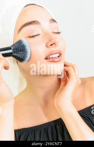 Una donna sta applicando il trucco con un pennello. Lei sorride ed è di buon umore Foto Stock